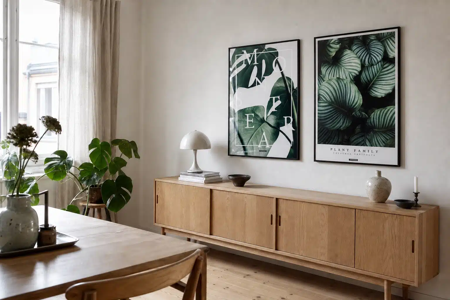 MONSTERA og CALATHEA ORBIFOLIA plakater i sorte rammer over en lys egetræsskænk i en dansk spisestue med naturligt dagslys.