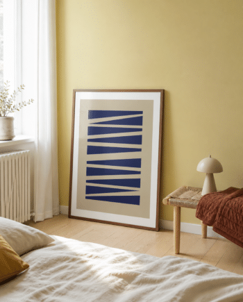 ABSTRAKT NO.1 plakat i valnødderamme i et lyst dansk soveværelse med gul væg, flettet bænk, rustfarvet tæppe og naturligt dagslys