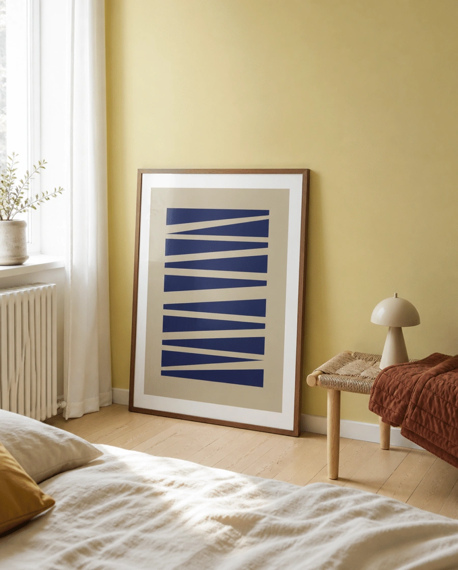 ABSTRAKT NO.1 plakat i valnødderamme i et lyst dansk soveværelse med gul væg, flettet bænk, rustfarvet tæppe og naturligt dagslys