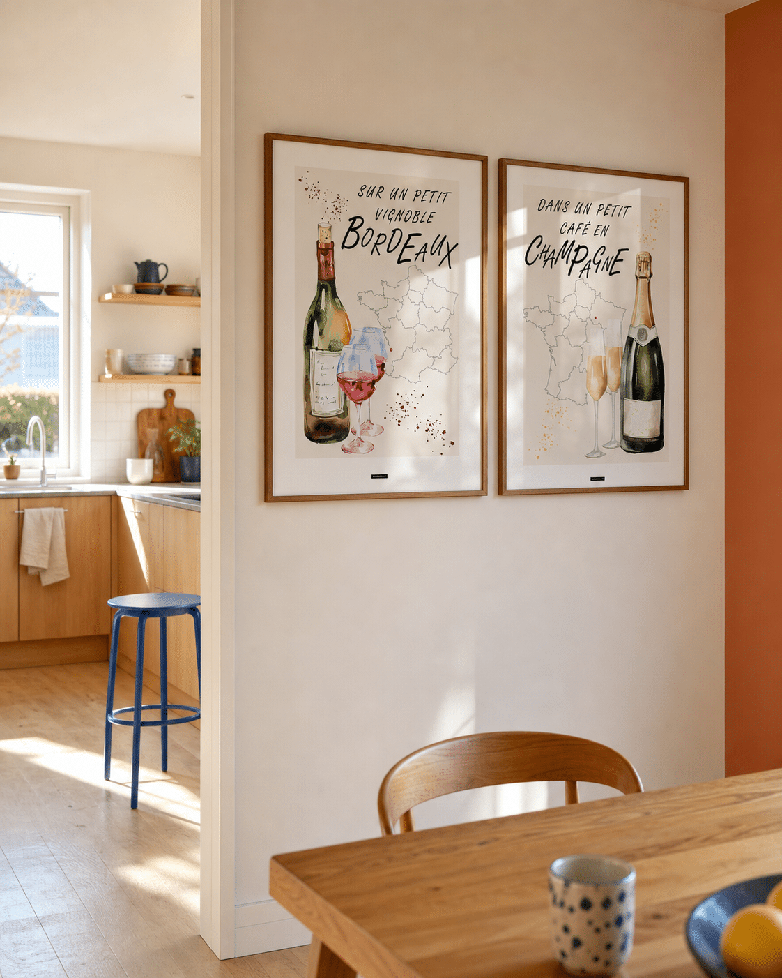 BORDEAUX NO.1 og CHAMPAGNE NO.1 plakater i valnødderammer i en lys dansk køkkenspisestue med egetræsskabe, blå stol, spisebord og dagslys