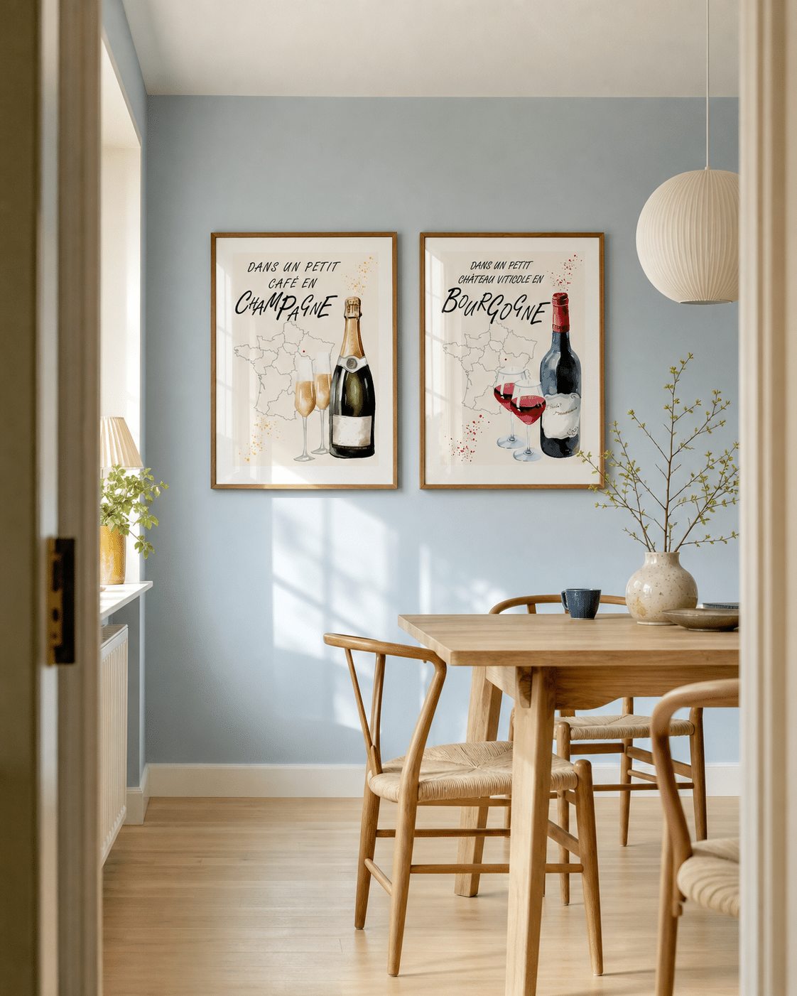 CHAMPAGNE NO.1 og BOURGOGNE NO.1 plakater i valnødderammer i en lys dansk spisestue med lyseblå væg, egetræsbord, papirpendel og dagslys