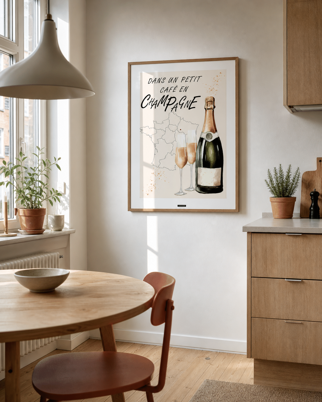 CHAMPAGNE NO.1 plakat i valnøddefarvet ramme i en lys dansk køkkenspisestue med egetræsskabe, terracotta stol, rundt bord og dagslys
