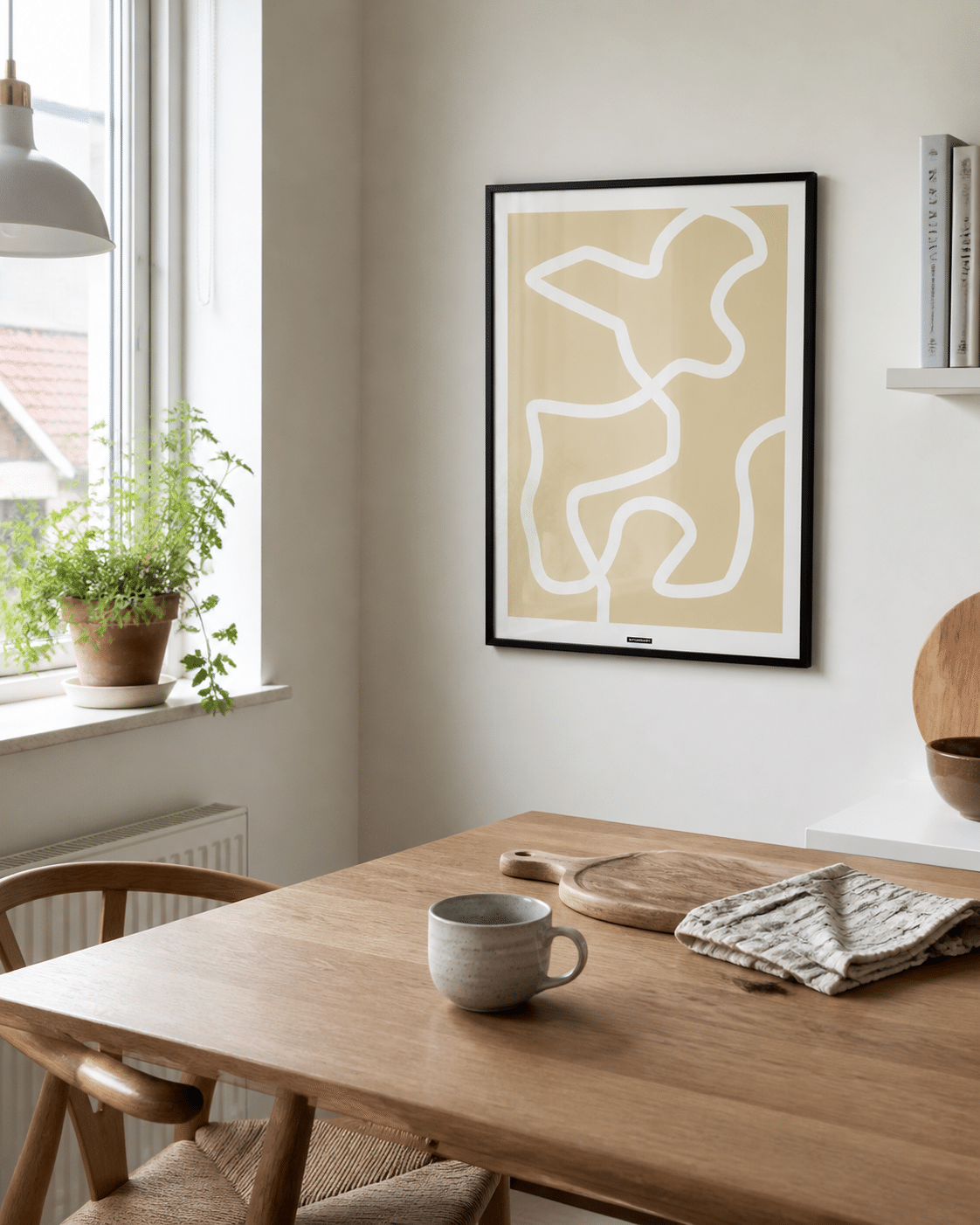 Lines No.2-plakaten med lyst grafisk linjemotiv i sort ramme hænger på en lys væg i en naturlig dansk køkkenkrog med træbord og dagslys.