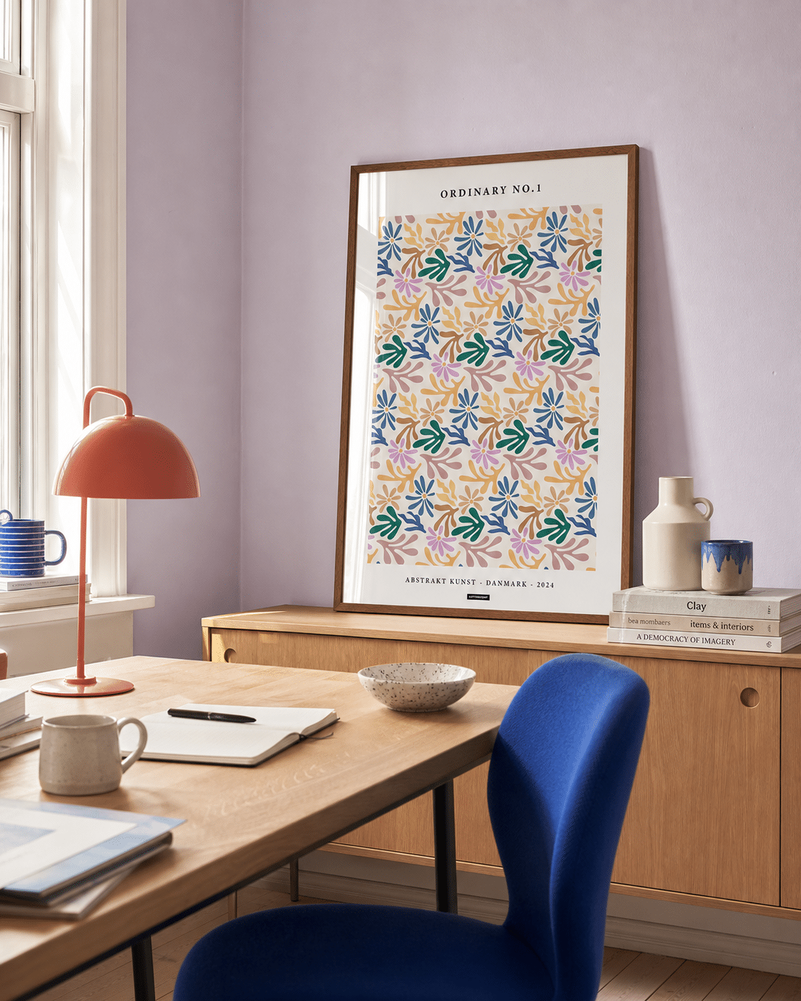 ORDINARY NO.1 plakat i valnøddefarvet ramme i et lyst dansk kontor med lavendelvæg, egetræsbord, blå stol og naturligt dagslys