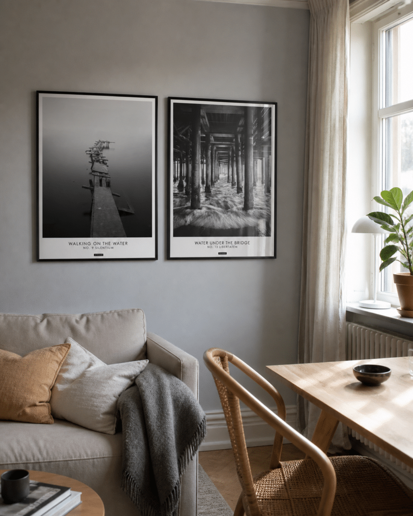 Silentium miljøbillede living room KASPERBENJAMIN Silentium og Libertatem plakater i sorte rammer hænger sammen på en lys væg i en naturlig dansk stue med sofa, spisebord, vindue og blødt dagslys.